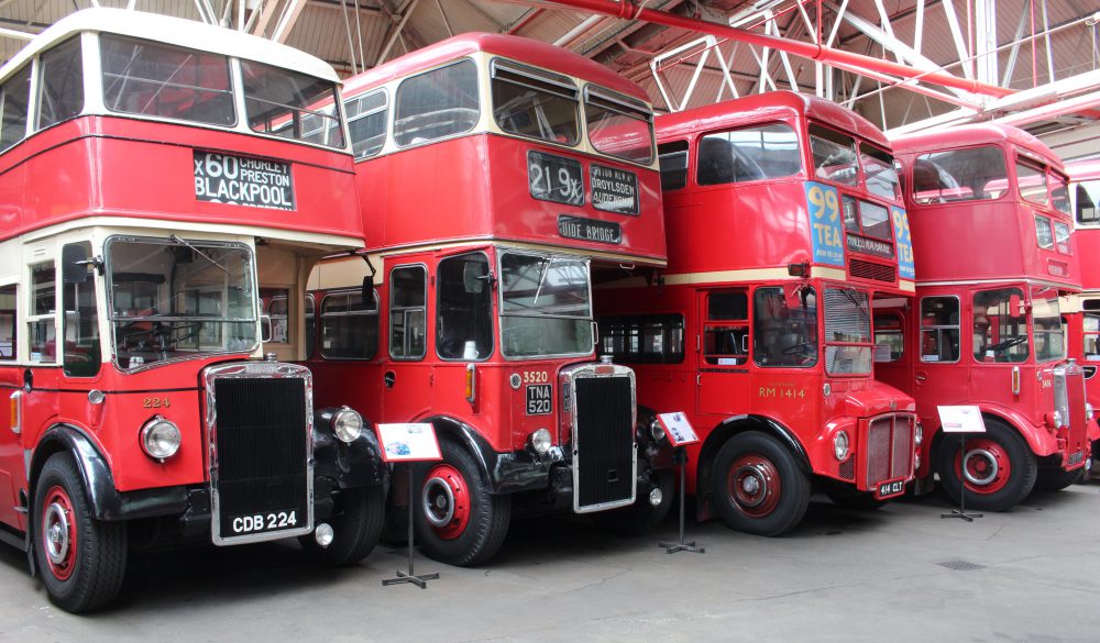 Four red double decker buses in a row inside a garage