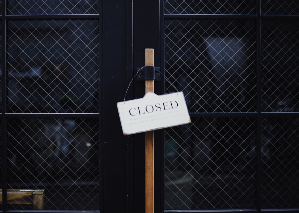 Black glazed doors with a closed sign hanging from the wooden handle
