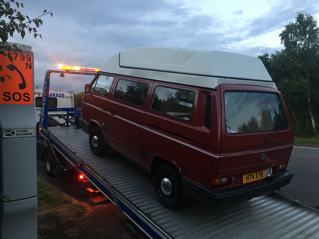 A red VW camper van being winched onto a trailer