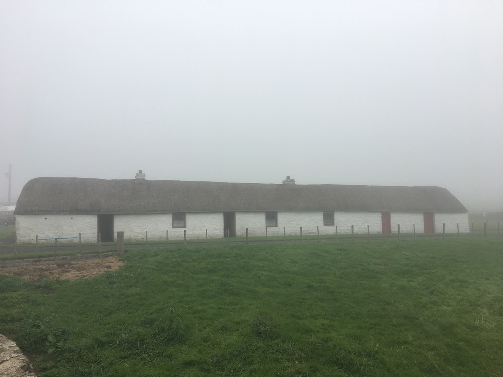 Laidhay Croft Museum, a single storey white building with a thatched roof, seen through a light mist.